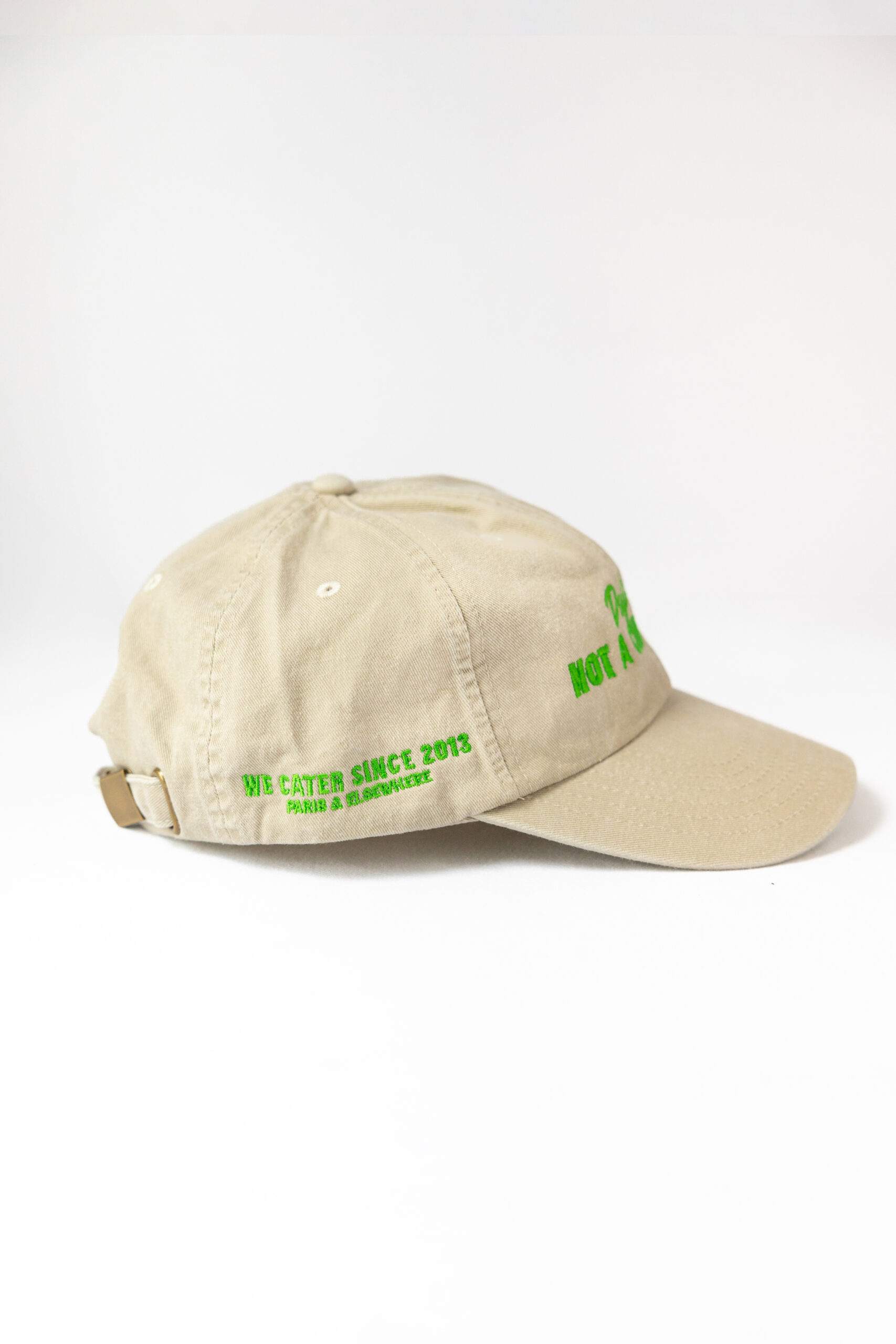 Le visuel montre une casquette beige de vue de côté. Le style vestimentaire est décontracté et cool et l'on voit une broderie verte indiquant « We cater since 2013. Paris & Elsewhere. », un clin d'oeil à l'activité du traiteur Chicken Bacon Lettuce.