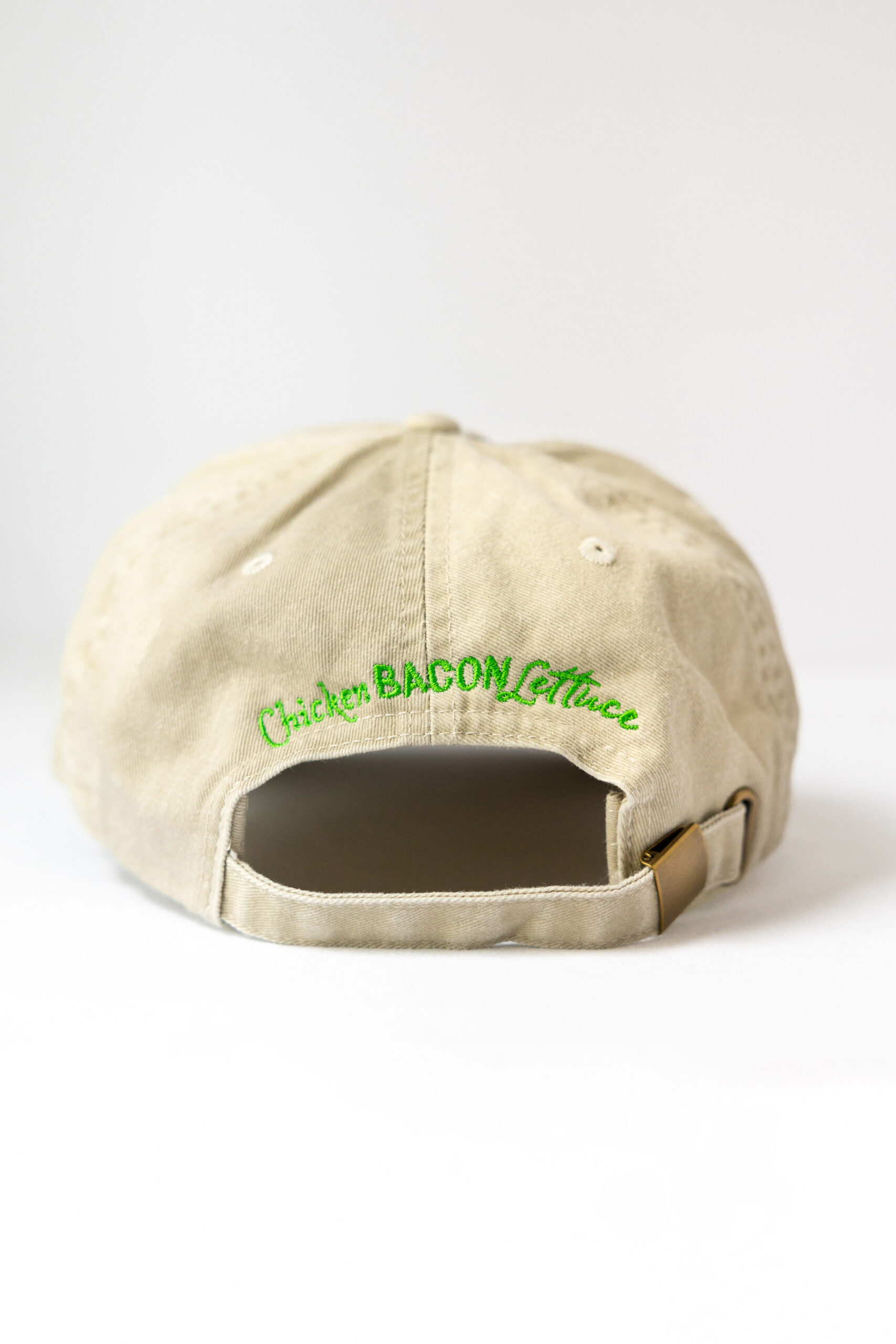 Le visuel montre une casquette beige de vue de dos. Le style vestimentaire est décontracté et cool et l'on voit une broderie verte indiquant « Chicken Bacon Lettuce », le logo du traiteur événementiel parisien CBL.