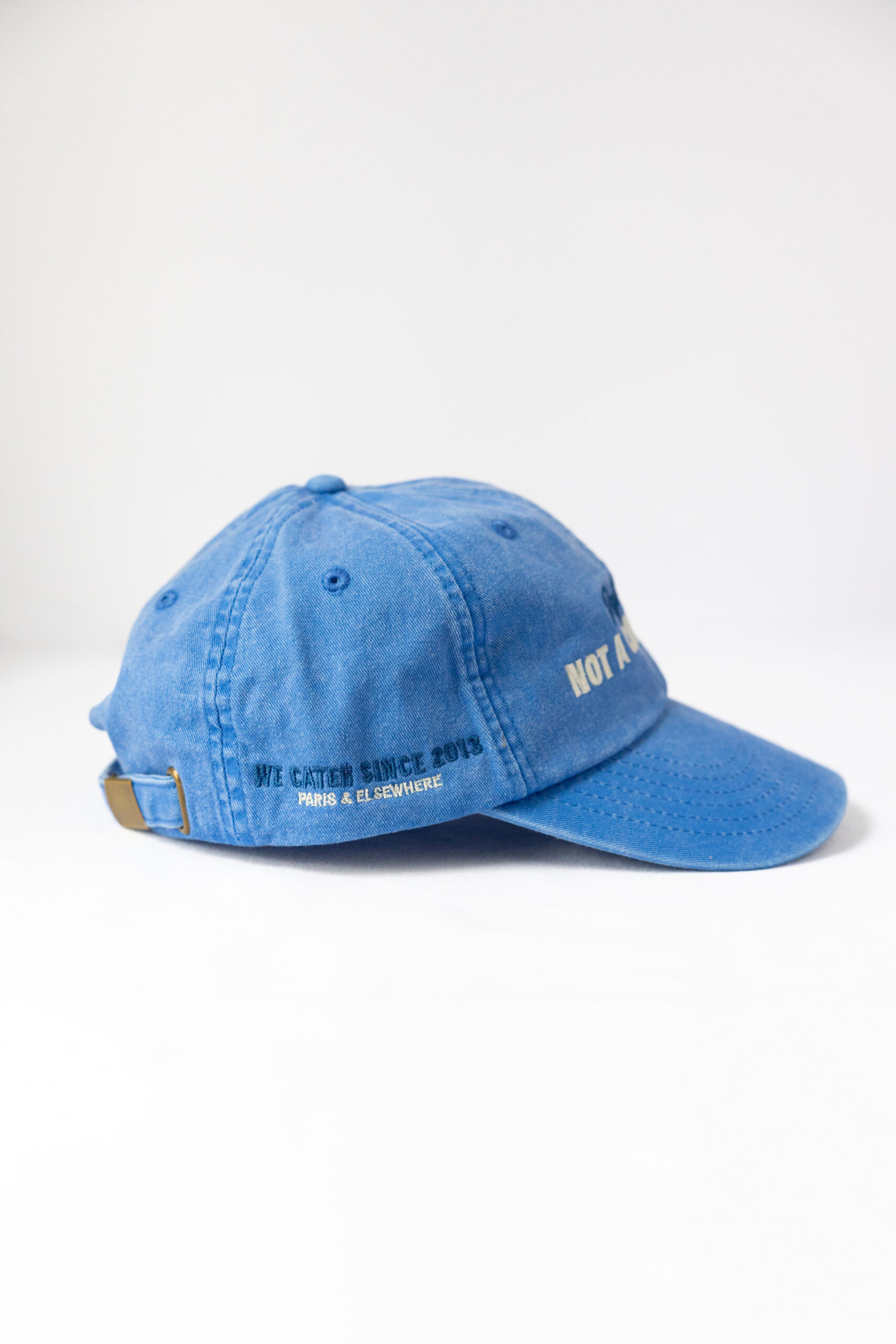 Le visuel montre une casquette bleue de vue de côté. Le style vestimentaire est décontracté et cool et l'on voit une broderie blanche indiquant « We cater since 2013. Paris & Elsewhere. », un clin d'oeil à l'activité du traiteur Chicken Bacon Lettuce.