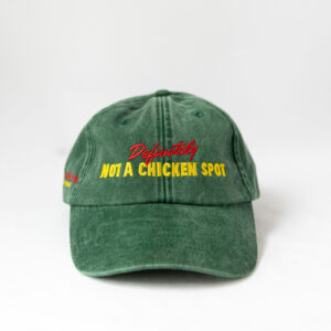 Le visuel montre une casquette verte de vue de face. Le style vestimentaire est décontracté et cool et l'on voit une broderie jaune et rouge sur le devant indiquant « Definitely Not a Chicken Spot », un clin d'oeil au nom du traiteur Chicken Bacon Lettuce.