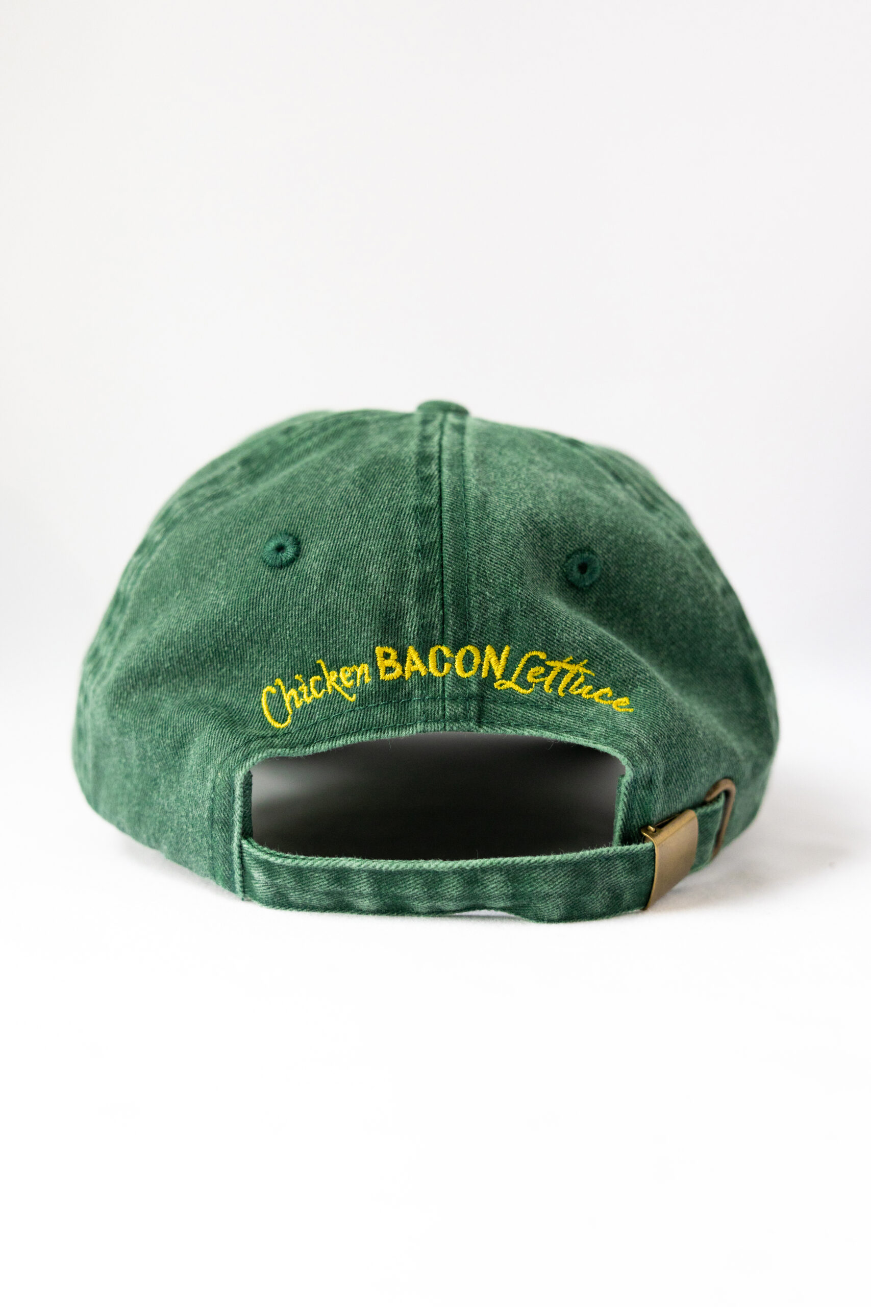 Le visuel montre quelqu’un de dos. La personne porte une casquette à l’envers. La casquette est verte. Le style vestimentaire est décontracté et cool et l'on voit une broderie jaune et rouge sur le devant indiquant « Definitely Not a Chicken Spot », un clin d'oeil au nom du traiteur Chicken Bacon Lettuce.