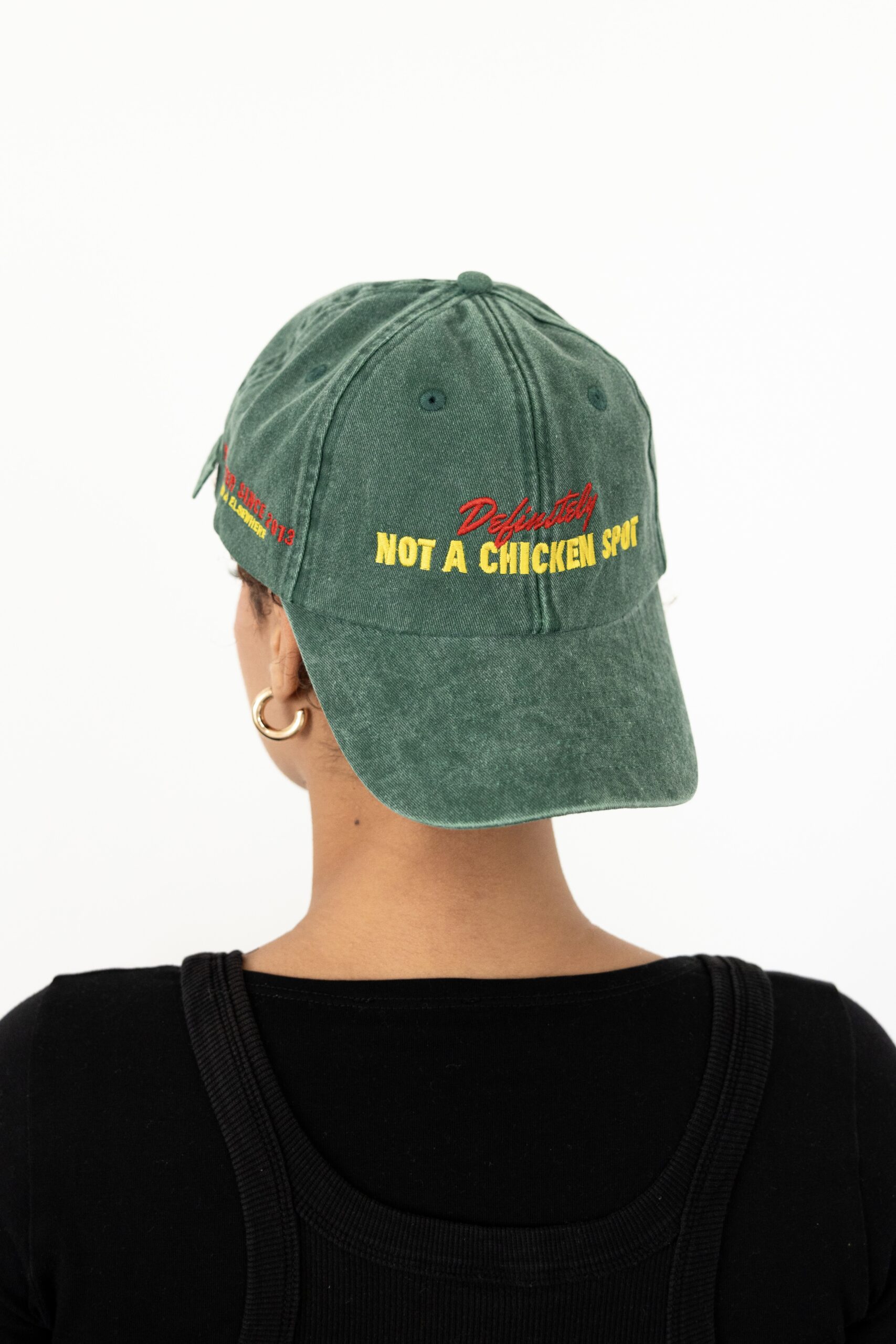 Le visuel montre quelqu’un de dos. La personne porte une casquette à l’envers. La casquette est verte. Le style vestimentaire est décontracté et cool et l'on voit une broderie jaune et rouge sur le devant indiquant « Definitely Not a Chicken Spot », un clin d'oeil au nom du traiteur Chicken Bacon Lettuce.