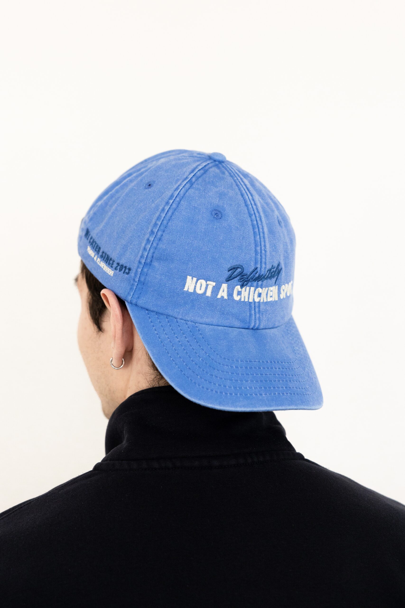 Le visuel montre quelqu’un de dos. La personne porte une casquette à l’envers. La casquette est bleue. Le style vestimentaire est décontracté et cool et l'on voit une broderie blanche sur le devant indiquant « Definitely Not a Chicken Spot », un clin d'oeil au nom du traiteur Chicken Bacon Lettuce.
